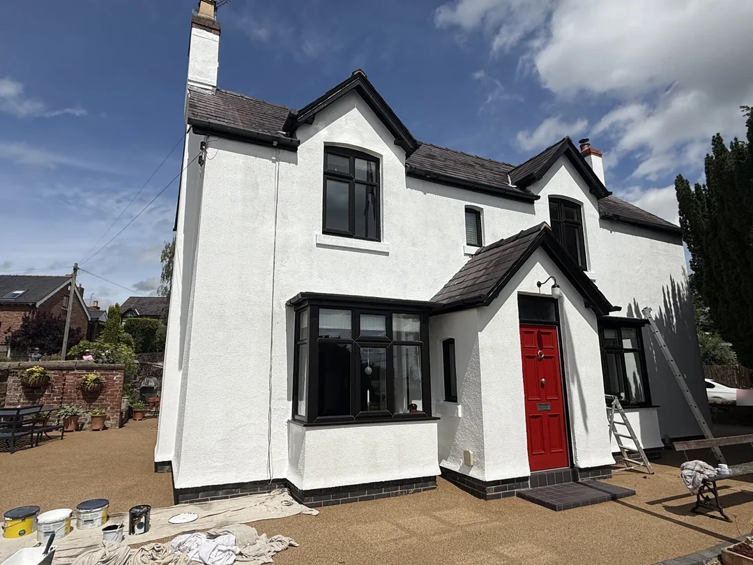 The front elevation with white render, black detailing and a red entrance door.